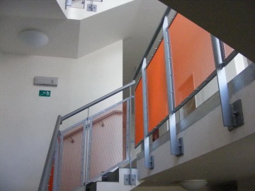 Schodiště s oranžovým zábradlím a únikovým značením na světlé zdi na sídlišti Milíčovský háj.