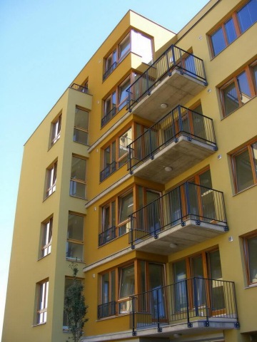 Moderní žlutá bytová budova Vokovice s balkony a velkými okny pod modrou oblohou.