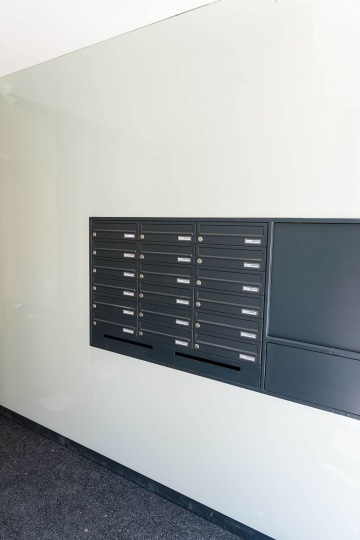 Černé poštovní schránky na bílé stěně v moderní budově Rezidence MAISON Ořechovka.