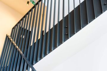 Kovové schodišťové zábradlí s moderním designem ve světlém interiéru Rezidence MAISON Ořechovka.