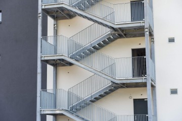 Venkovní kovové schodiště na bílém pozadí budovy AFI Home Kolbenova.