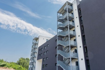 Vícepodlažní budova AFI Home Kolbenova s venkovním ocelovým schodištěm a jasnou modrou oblohou.