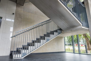 Moderní interiér AFI Home Třebešín se schodištěm z betonu a skla s výhledem na venkovní zeleň.