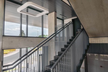 Moderní schodiště AFI Home Třebešín s kovovým zábradlím a velkými okny, výhled na venkovní křižovatku.