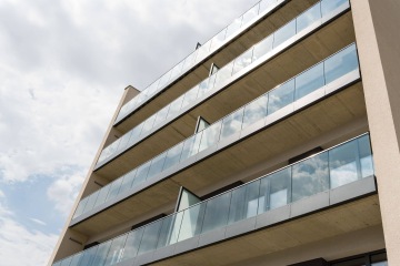 Moderní bytový dům AFI Home Třebešín s balkony se skleněnými zábradlími pod zamračenou oblohou.