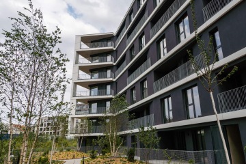 Moderní bytový dům v Rezidenční čtvrti Hagibor s balkony a mladými stromy v popředí, oblačné nebe.