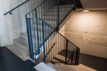 Betonové schodiště s kovovými madly ve veřejné budově v Rezidenční čtvrti Hagibor, úniková značka na zdi, moderní osvětlení.