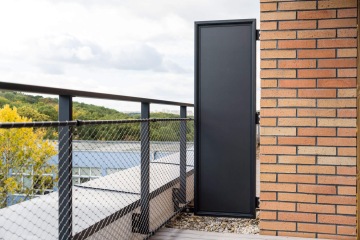 Balkón YIT Parvi Cibulka s kovovým zábradlím, cihlovou zdí a černou brankou, s výhledem na zelené stromy.