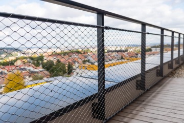 Drátěné zábradlí v YIT Parvi Cibulka s výhledem na rozostřené město a jasnou oblohu v pozadí.