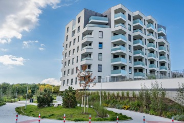 Moderní bytový dům v Britské Čtvrti s balkony a zeleným okolím pod modrým nebem.