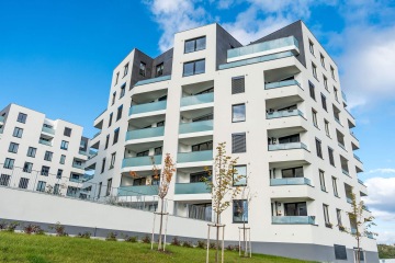 Moderní bytový dům v Britské Čtvrti s balkony a skleněnými zábradlími pod modrou oblohou.