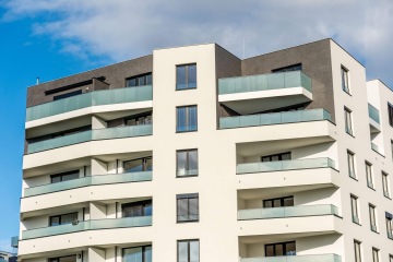 Moderní bytový dům v Britské Čtvrti s prosklenými balkony, modrá obloha v pozadí.