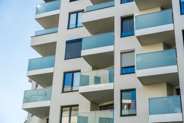 Moderní bytový dům v Britské Čtvrti s prosklenými balkony a modrými okny na světlé fasádě.