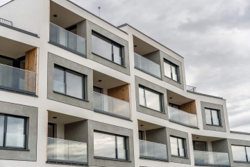 Moderní bytový dům Barrandez Vous s prosklenými balkony a šedobílou fasádou pod zataženou oblohou.