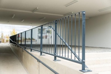 Černé kovové zábradlí pod přístřeškem v Barrandez Vous, vedle betonové rampy.