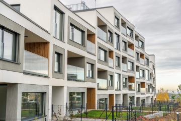Moderní bytový dům Barrandez Vous s balkony a velkými okny, obklopený trávníkem a oplocením.