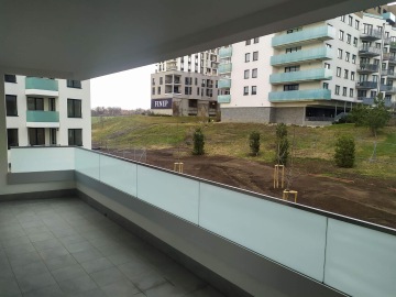 Balkon s výhledem na moderní bytové domy v Britské Čtvrti a zatravněné prostranství.