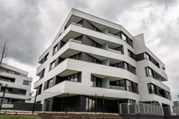 Moderní bílá bytová budova Rezidence U Sluncové s černými akcenty a balkony pod zamračenou oblohou.