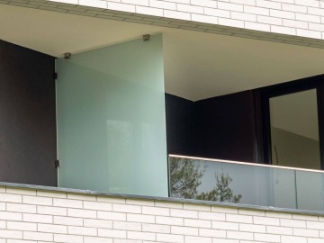 Prosklená balkónová zábrana Rezidence U Sluncové s mléčným sklem a černými rámy na moderní budově.