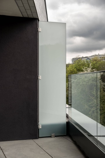 Skleněná zástěna Rezidence U Sluncové na moderním balkóně s výhledem na stromy a oblačné nebe.