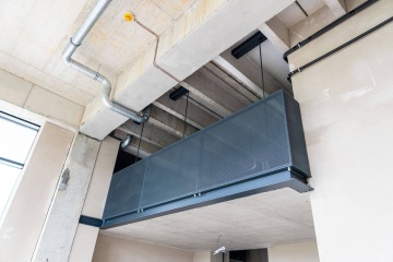 Drátěný balkon zavěšený na stropě moderního betonového interiéru Vanguard Praha s přívodním potrubím.