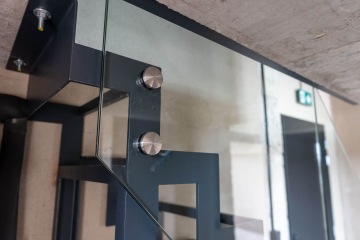 Montáž skleněného zábradlí s kovovými úchyty v moderním interiéru Vanguard Praha.