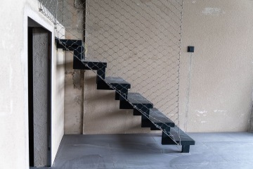 Moderní černé schodiště ve Vanguard Praha s kovovou mříží proti bílé stěně.