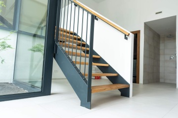 Schodiště s dřevěnými stupni a černým zábradlím v moderním interiéru Rezidence Erbenova s prosklenou stěnou.