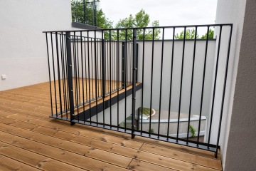 Dřevěná terasa Rezidence Erbenova s kovovým zábradlím, bílé stěny, pohled na zahradu v pozadí.