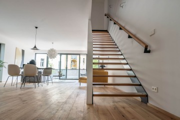 Moderní interiér Rezidence Erbenova s dřevěnými schody, jídelním stolem a židlemi, velká okna vpouštějí světlo.