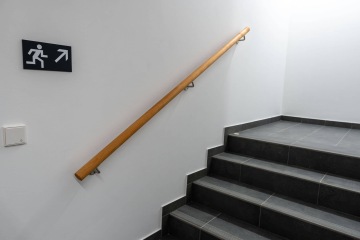 Bezpečnostní schodiště Rezidence Erbenova s dřevěným zábradlím a únikovým znakem na bílém pozadí.