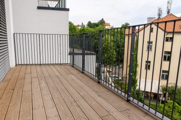 Moderní balkon Rezidence Erbenova s dřevěnou podlahou a kovovým zábradlím, výhled na okolní domy a zeleň.