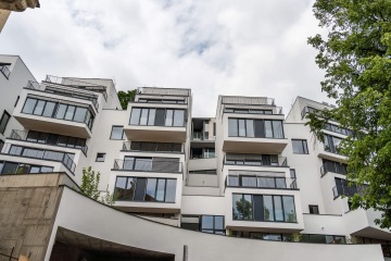 Moderní bytový dům Rezidence Erbenova s velkými okny a balkony, stromy v popředí a oblačná obloha.