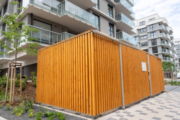 Dřevěná konstrukce v moderním bytovém komplexu v Britské Čtvrti s balkonem a nově vysazeným stromem na dlážděném chodníku.