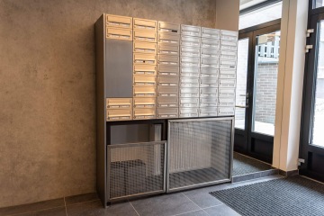 Kovové poštovní schránky v moderní chodbě Britské Čtvrti vedle skleněných dveří.