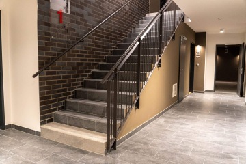 Chodba v Britské Čtvrti s šedými dlaždicemi, schodištěm s kovovým zábradlím a dveřmi označenými číslem 108.