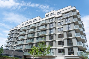 Moderní obytná budova v Britské Čtvrti s balkony a prosklenou fasádou pod jasnou modrou oblohou.