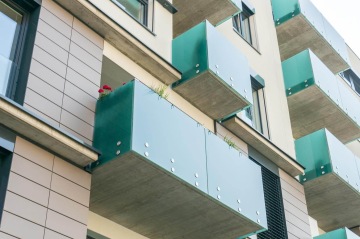 Moderní budova BD Smart s balkóny se zelenými skleněnými zábradlími a květinami.