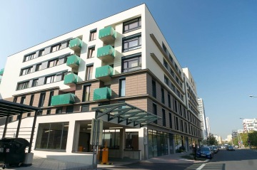 Moderní bytový dům BD Smart s balkony, vedle klidné ulice pod modrou oblohou.