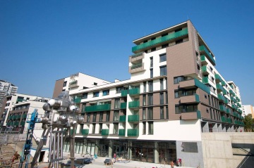 Moderní bytový dům BD Smart s balkony a uměleckou instalací na modré obloze.