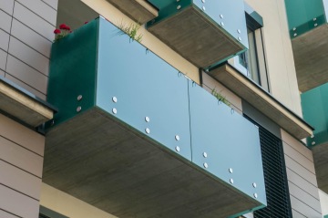 Moderní balkony se zeleným celoskleněným zábradlím na bytové budově.