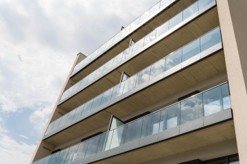 Moderní bytový dům s balkony s celoskleněným zábradlím.