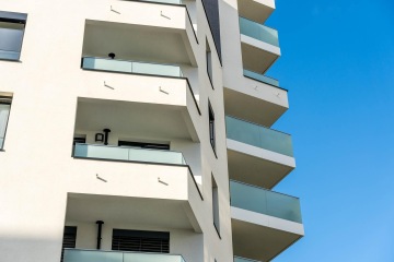 Moderní bytový dům s balkony s celoskleněným zábradlím proti modré obloze.