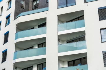 Moderní bytový dům s balkony se celoskleněným zábradlím.