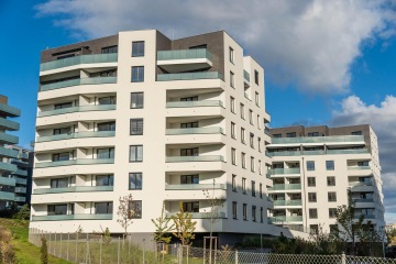 Moderní bytový komplex s balkony s celoskleněným zábradlím pod modrou oblohou.