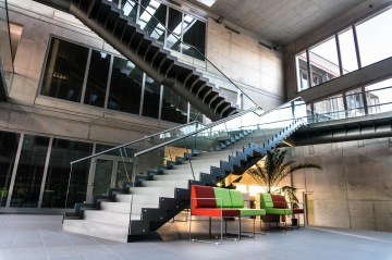 Moderní interiér s designovým schodištěm s celoskleněným zábradlím a barevnými sedačkami.