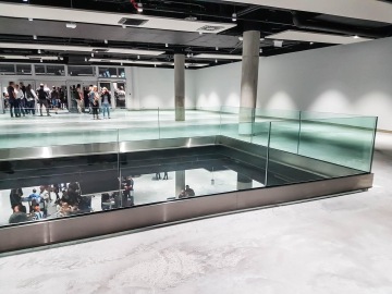 Moderní interiér s celoskleněným zábradlím, lidé na různých úrovních prostorově propojeného otevřeného plánu.