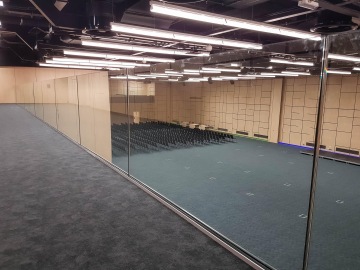 Velká prázdná konferenční místnost s řadami prázdných židlí, prosklená stěna a stropní osvětlení.