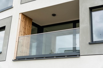 Balkón moderní budovy s celoskleněným zábradlím a dřevěnými obklady.