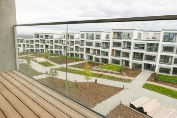Moderní bytová výstavba s upravenými zahradami a balkony s celoskleněným zábradlím.